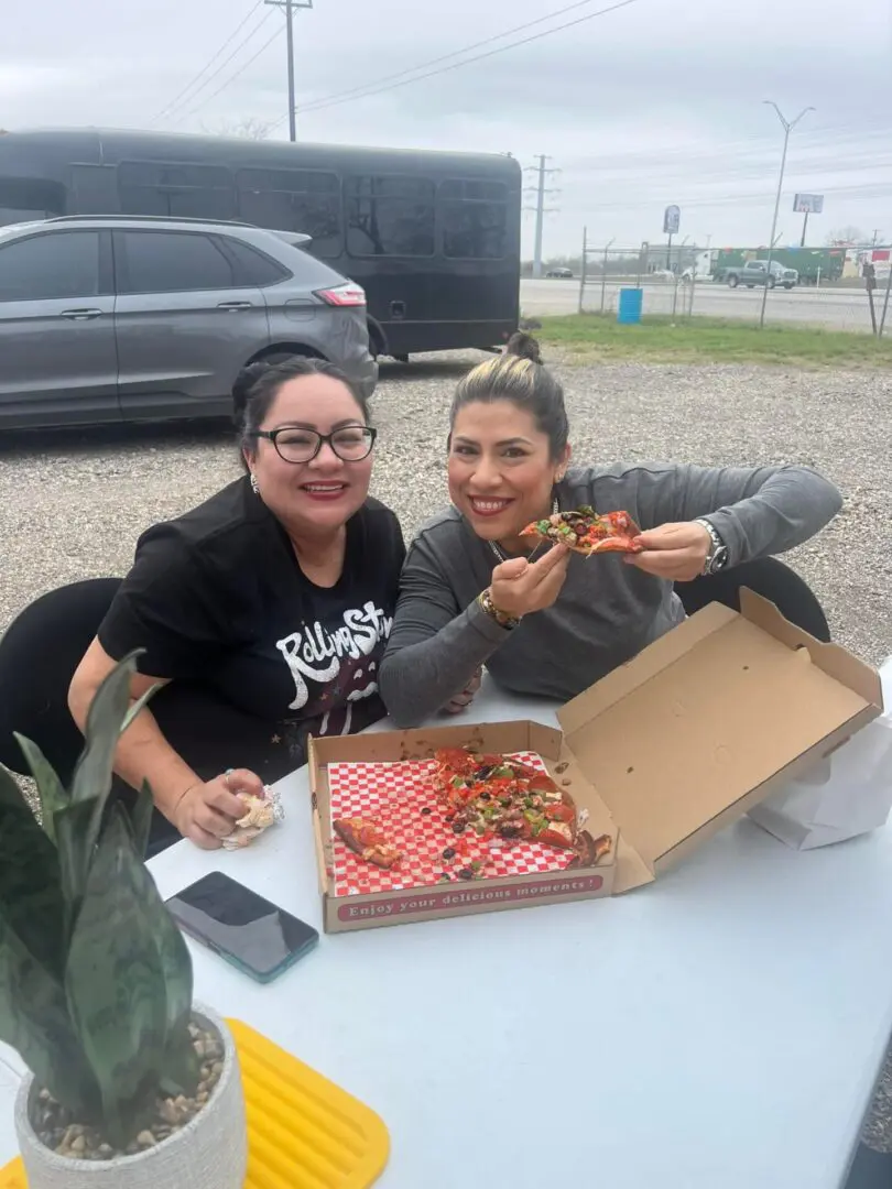 Two women enjoying pizza outdoors together.